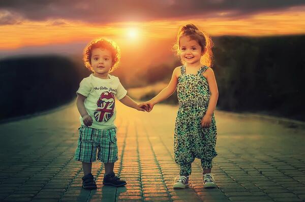 Bild vergrößern: Zwei Kinder vor einem Sonnenuntergang, die sich an der Hand halten.